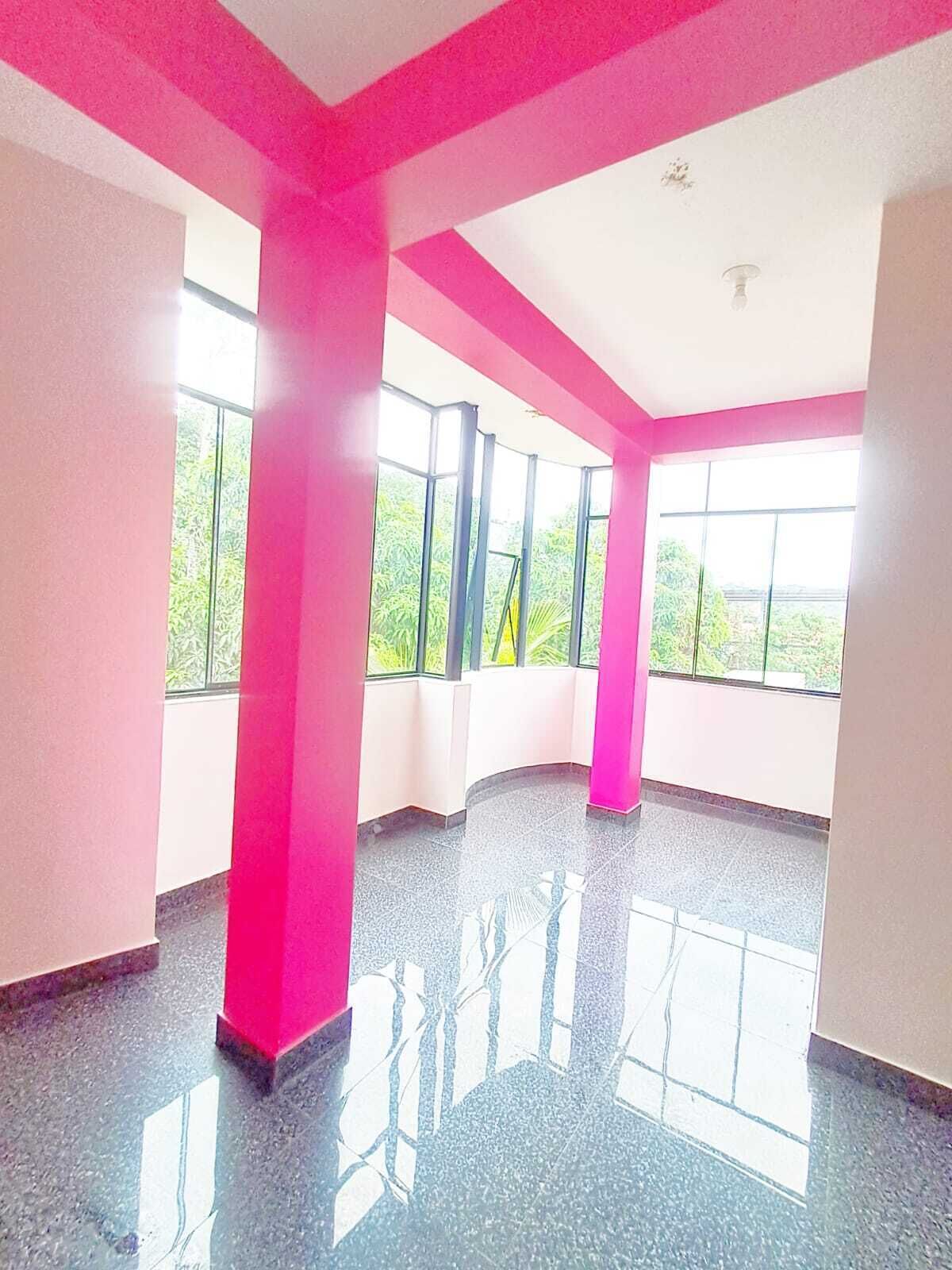 A spacious room with large windows, a polished floor, and a pink accent wall.