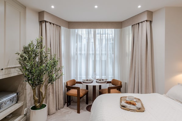 Ein Hotelzimmer mit Bett, einem Esstisch mit Stühlen, einer Zimmerpflanze und einem Tisch mit einer Essschale.