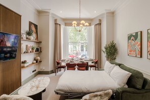 Ein Hotelzimmer mit einem großen Bett, einem Esstisch für vier Personen, einem Fernseher und Kunstwerken an den Wänden.