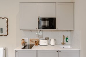 Eine Küche mit weißen Schränken, einer schwarzen Mikrowelle, einem weißen Toaster, einer Kaffeemaschine und einem Waschbecken mit goldenem Wasserhahn.