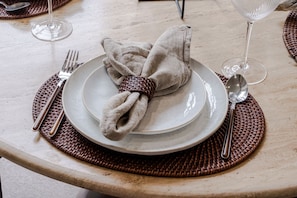 Ein gedeckter Tisch mit gefalteter Serviette, einem Teller, einer Gabel, einem Löffel und einem Weinglas.
