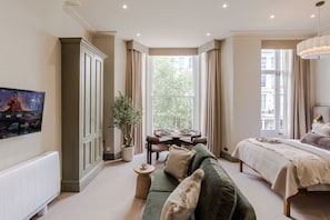Ein Schlafzimmer mit Bett, einem grünen Sofa, einem Esstisch und einem großen Fenster.