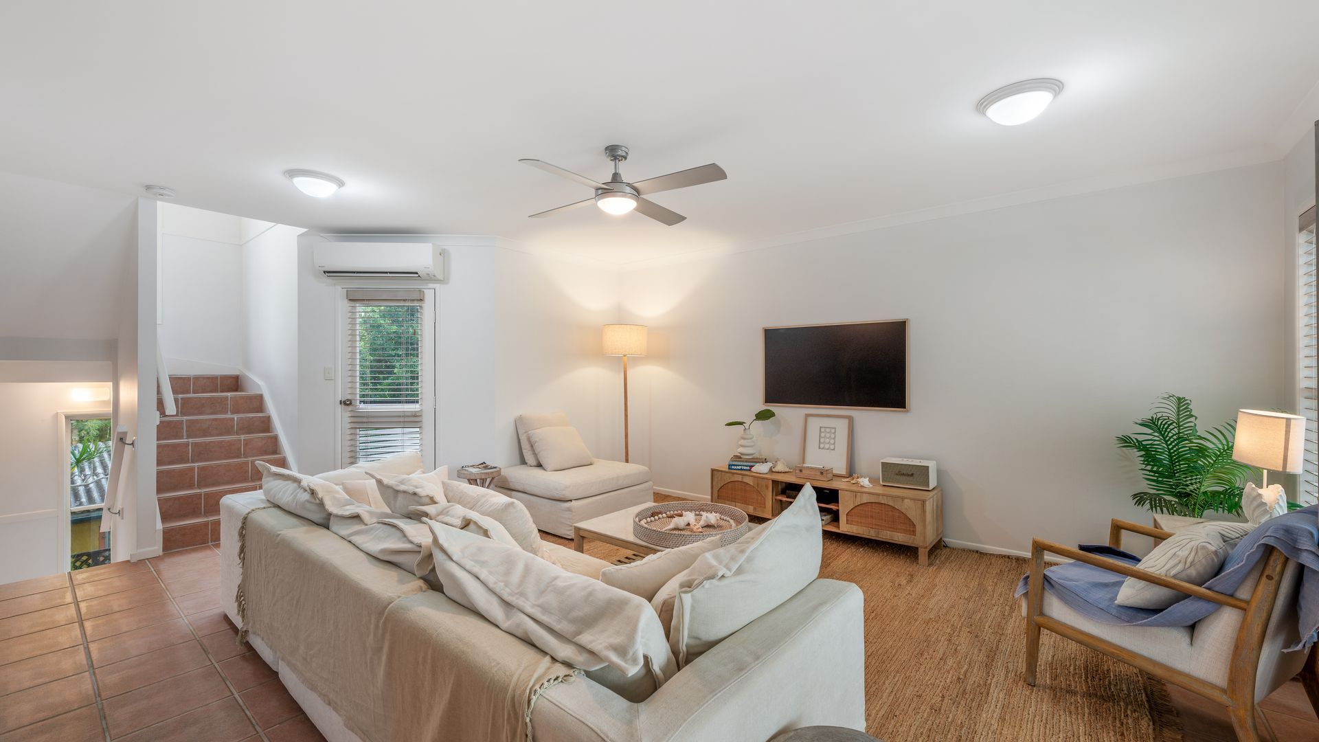 Ein Wohnzimmer mit einer Couch, einem Couchtisch, einer Lampe, einem Fernseher und einem Deckenventilator.