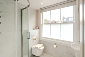 A bathroom with a glass shower enclosure, a toilet, a sink, and a large window with a city view. - Your Apartment - Earl's Court | Studio - Top floor (London)