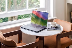 A laptop on a table by a window with a cup and glasses. - Your Apartment - Earl's Court | Studio - Top floor (London)
