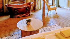 A rustic room with a bathtub, a chair, a round table, and a bed with towels. - 8 Henham Barns, Henham Park, Nr Southwold, Suffolk (Suffolk)