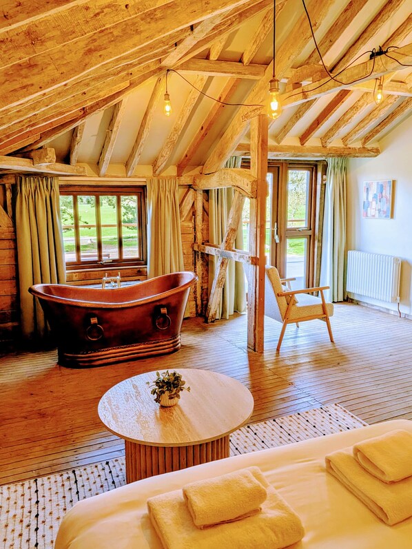 Ein rustikales Zimmer mit Badewanne, Stuhl, rundem Tisch und einem Bett mit Handtüchern.