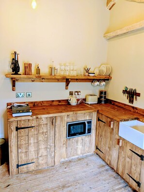 A kitchen with wooden cabinets, a microwave, a coffee maker, and various kitchen utensils. - 8 Henham Barns, Henham Park, Nr Southwold, Suffolk (Suffolk)