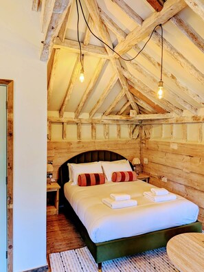 Ein Schlafzimmer mit Holzbalkendecke, einem Bett mit weißen Leinen und zwei Nachttischlampen.