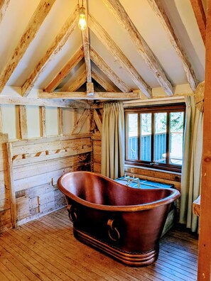 Ein rustikaler Raum mit freiliegenden Holzbalken, einer antiken Badewanne und einem Fenster mit Vorhängen.