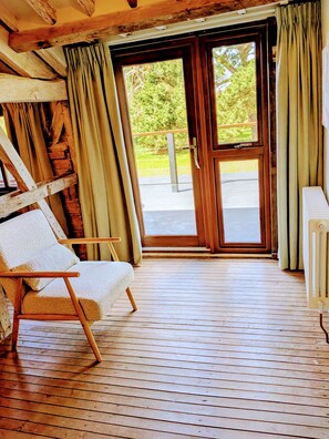 A wooden-framed room with a sliding glass door leading outside, a white cushioned chair, and a radiator. - 8 Henham Barns, Henham Park, Nr Southwold, Suffolk (Suffolk)
