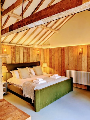 Un dormitorio con techo de madera, cama verde, ropa de cama blanca y un radiador.