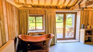 A rustic room with a large bathtub, wooden walls, and a view of a garden through a sliding door. - 6 Henham Barns, Henham Park, Nr Southwold, Suffolk (Suffolk)