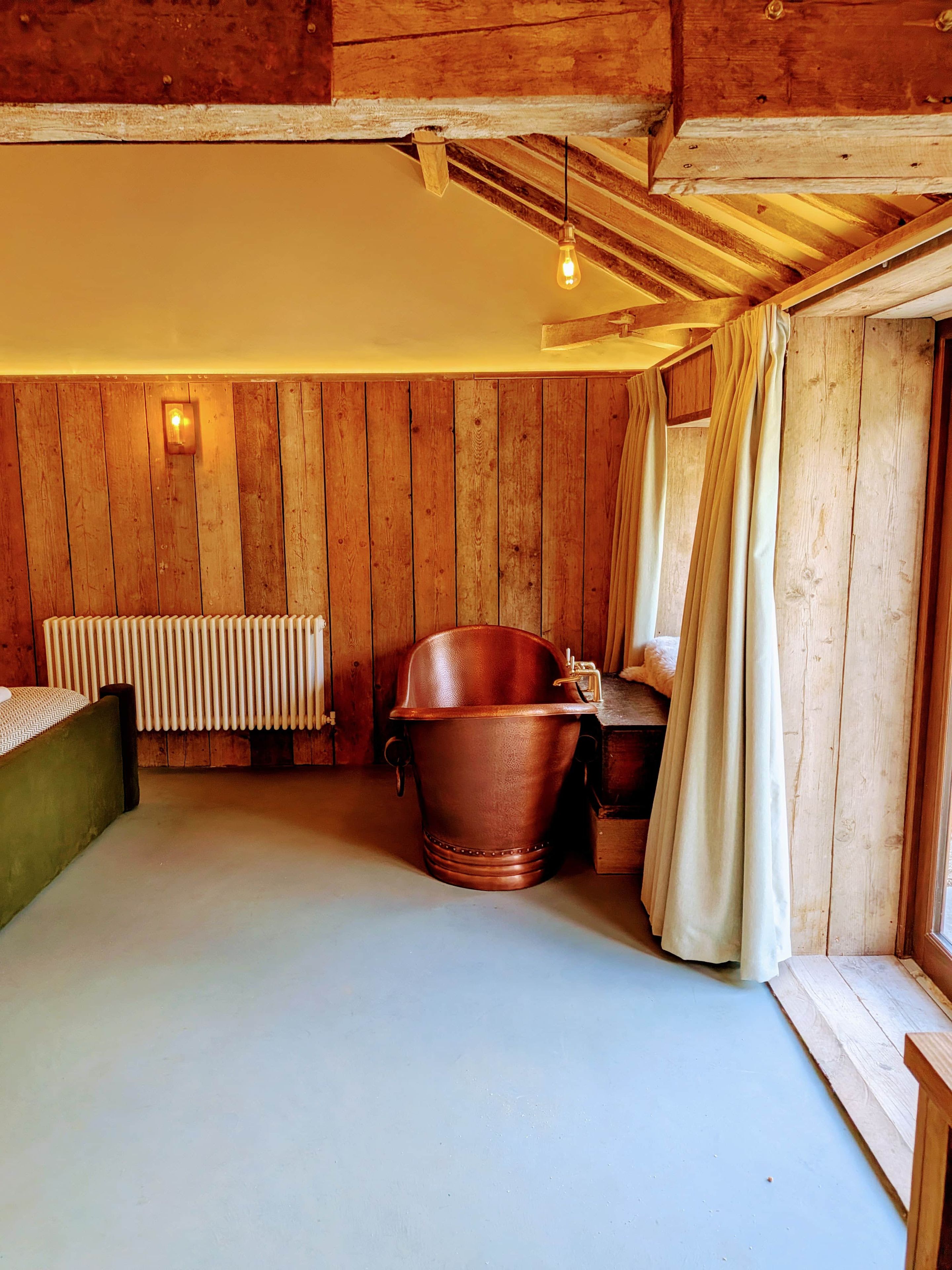 Ein rustikaler Holzraum mit einer großen Badewanne, einem Heizkörper und einem mit Vorhängen drapierten Fenster.