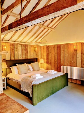 Un dormitorio con techo de madera, cama verde, ropa de cama blanca y un radiador.