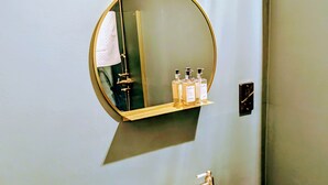 A bathroom with a white sink, a wooden vanity, a round mirror, and toiletries on a shelf. - 6 Henham Barns, Henham Park, Nr Southwold, Suffolk (Suffolk)