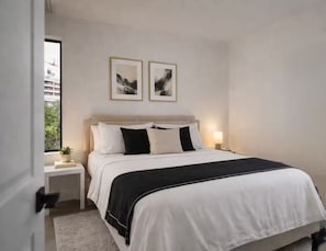 Une chambre à coucher avec un lit, des tables de chevet, une commode, une fenêtre et deux tableaux encadrés accrochés au mur.