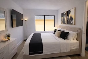 Une chambre moderne avec un grand lit, des lampes de chevet, un téléviseur à écran plat et des œuvres d’art accrochées aux murs.