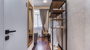 Un pasillo con piso de madera, un armario con espejo, una zona de estar con una silla y una percha para ropa.