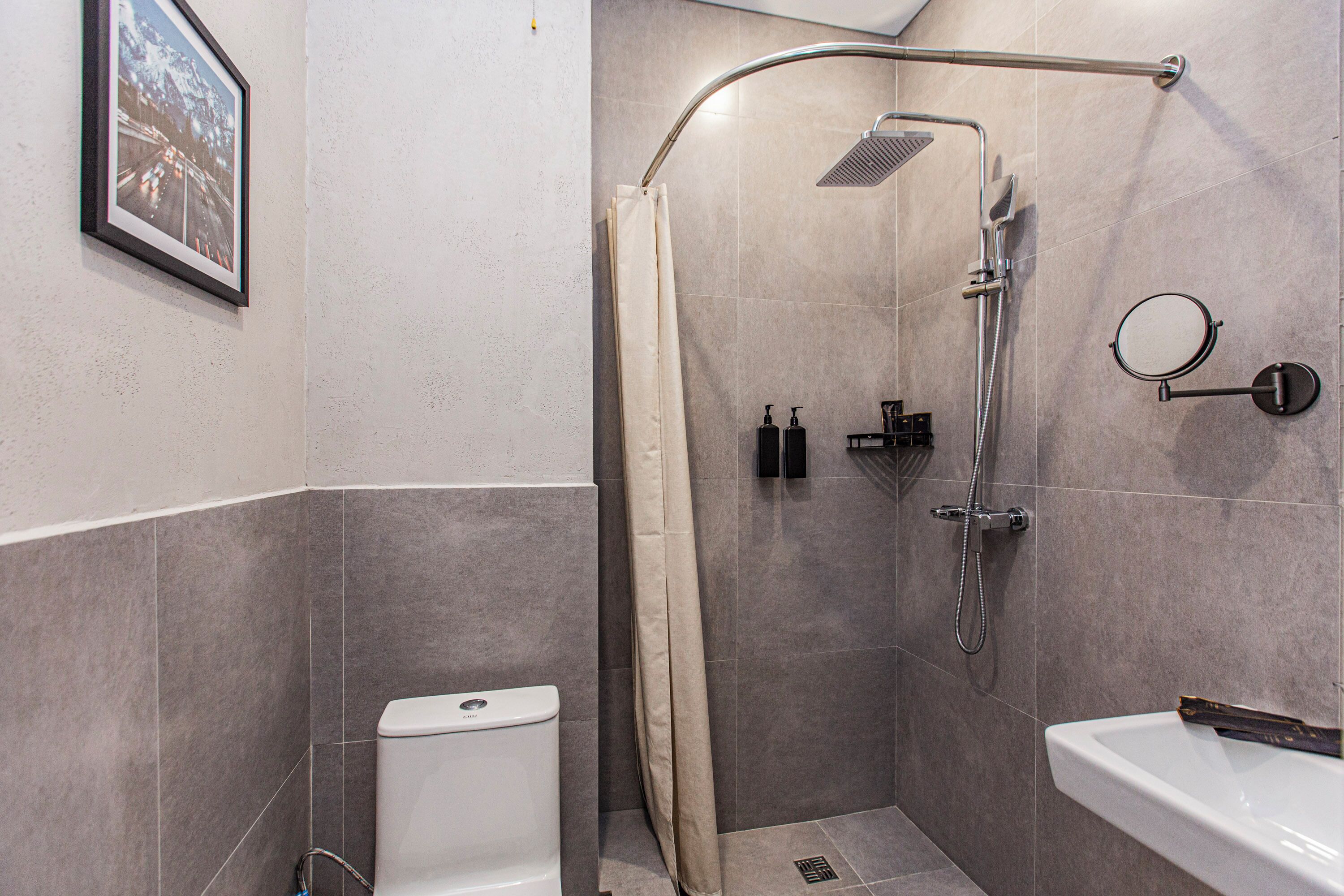 A bathroom with a shower, toilet, sink, and a framed picture on the wall.