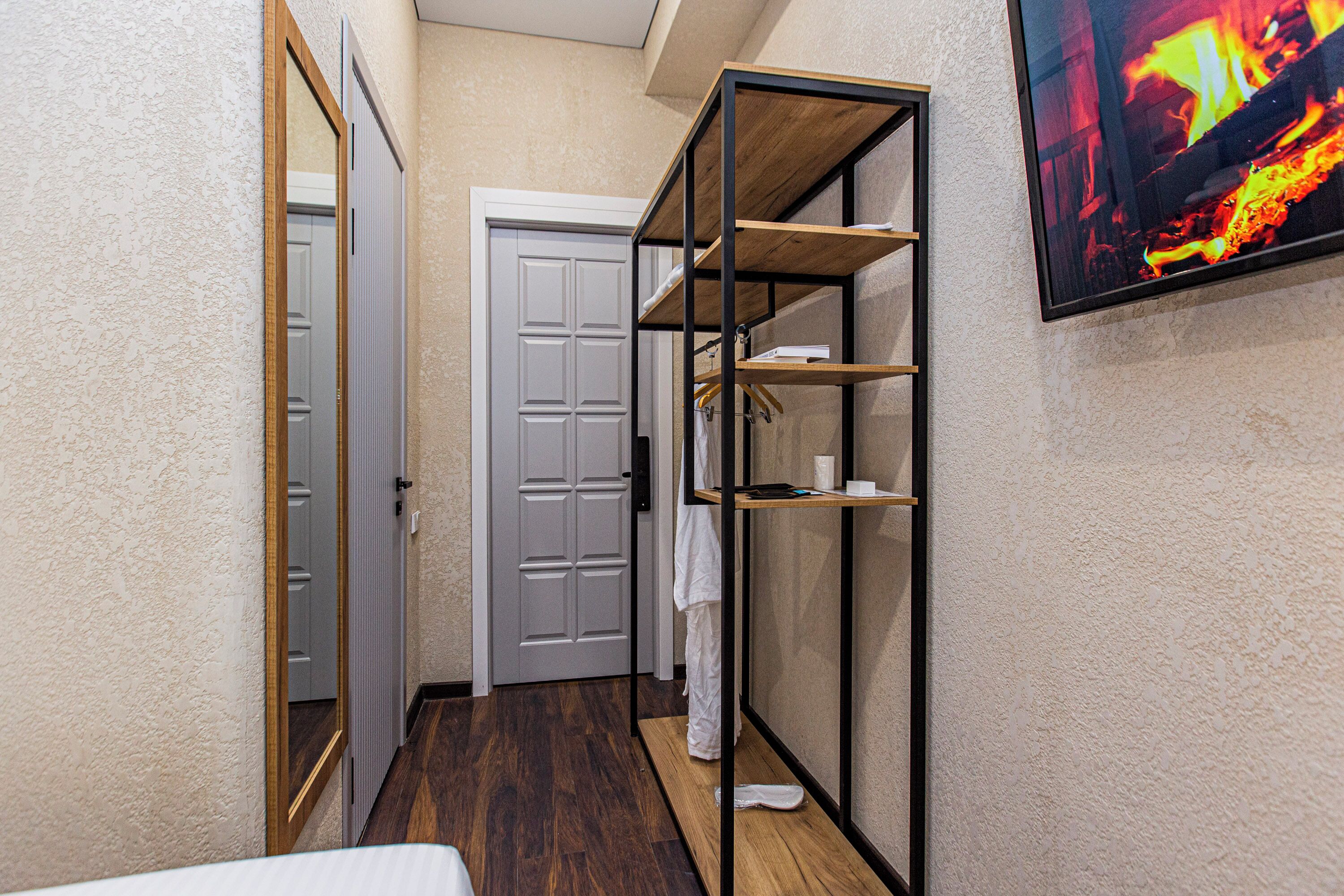 Un couloir avec un plancher en bois, une porte blanche et une étagère métallique adossée au mur.