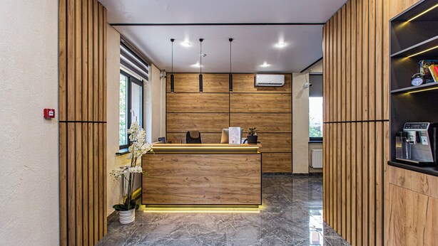 Una recepción con mostrador de madera, una orquídea en maceta y una máquina de café a la derecha.