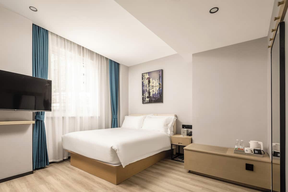 A hotel room with a bed, a TV, a nightstand, a coffee maker, and a painting on the wall.