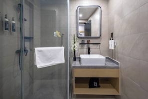 Un baño moderno con cabina de ducha de vidrio, un lavamanos blanco, un espejo y artículos de aseo en la pared.