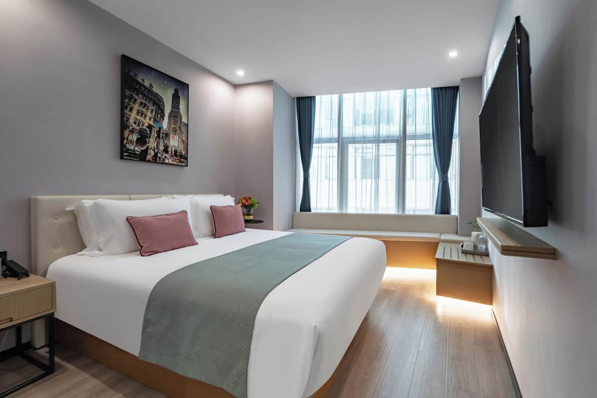 A hotel room with a large bed, a flat-screen TV, a window with curtains, and a painting on the wall.