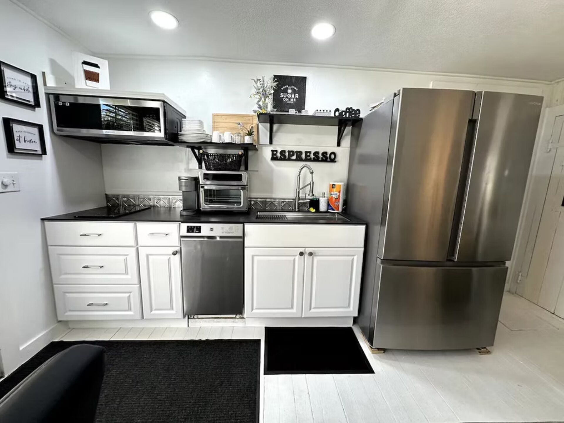 Una cocina moderna con armarios blancos, un refrigerador de acero inoxidable, una cafetera y una estación de espresso.