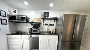 Uma cozinha moderna com armários brancos, uma geladeira de aço inoxidável, uma máquina de café e um espaço para café expresso.