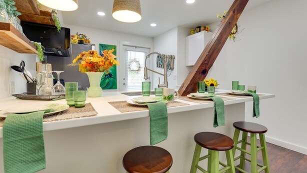 Een keuken met een centraal eiland, barstoelen, hangende lampen en een houten balk.