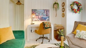 Een woonkamer met een groene bank, een gele fauteuil, een beige bank, een schilderij, een bureau, een hangplant en een krans aan de muur.