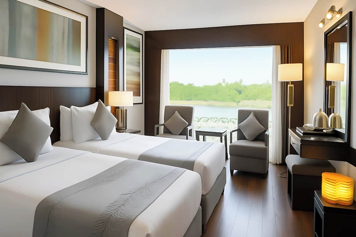 A hotel room with two beds, a desk, a chair, a lamp, and a view of a lake.