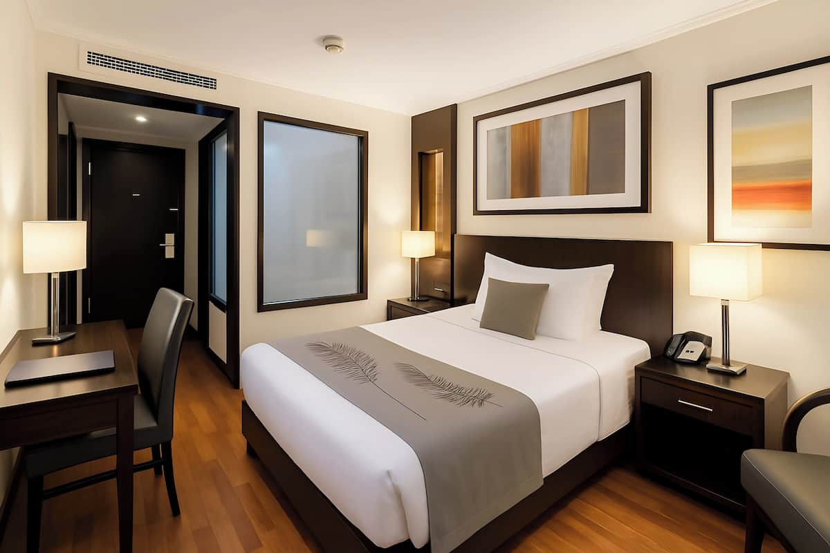 A hotel room with a large bed, a desk, a chair, a nightstand, and a wall-mounted TV.