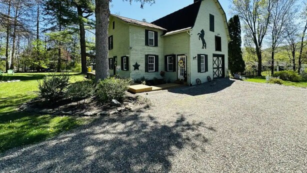 Une maison à deux étages avec une grande véranda à l’avant, un garage et une allée menant à l’entrée.