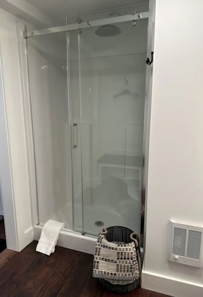 Une douche fermée par des parois de verre, avec une serviette sur le sol et un panier à côté.