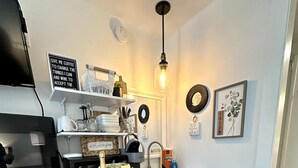 Une cuisine compacte avec un plan de travail blanc, un petit réfrigérateur, un évier et un luminaire suspendu.