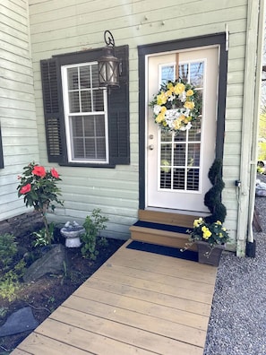 Une maison avec une porte d’entrée, un petit porche, un arrangement floral et une plante en pot.