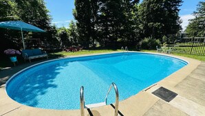 Une piscine d’un bleu éclatant, avec des échelles en métal, entourée d’une terrasse en béton et d’une clôture.