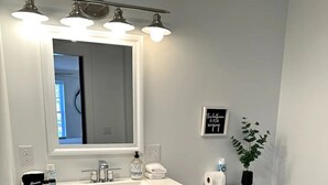 Une salle de bain avec un meuble-lavabo blanc, un grand miroir, des toilettes et une plante en pot.