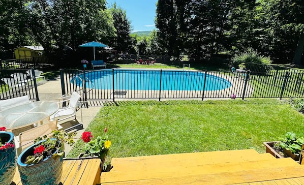 Un jardin avec une piscine, une terrasse en bois et une zone délimitée par une clôture.