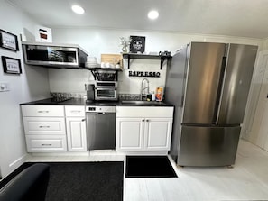 Una cocina moderna con armarios blancos, un refrigerador de acero inoxidable, una cafetera y una estación de espresso.