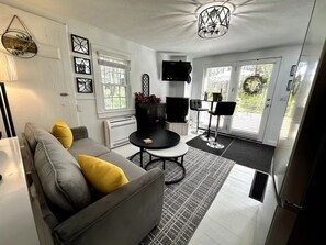 Una sala de estar moderna con un sofá gris, cojines amarillos, una mesa redonda de centro y un mueble de TV negro.