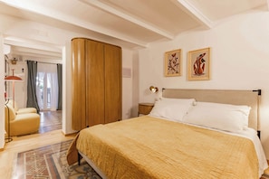 Un dormitorio con una cama, un armario, una silla y dos obras de arte colgadas en la pared.