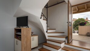Eine Treppe mit Holzstufen führt zu einem Balkon, ein Fernseher steht auf einer Holzeinrichtung, und es bietet sich ein Blick ins Freie.
