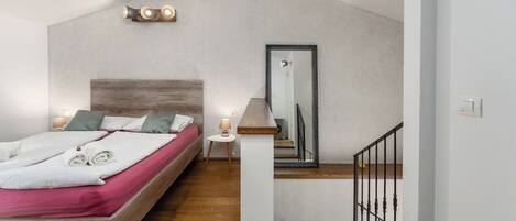 A bedroom with a wooden bed, a nightstand, a lamp, a mirror, and a staircase.