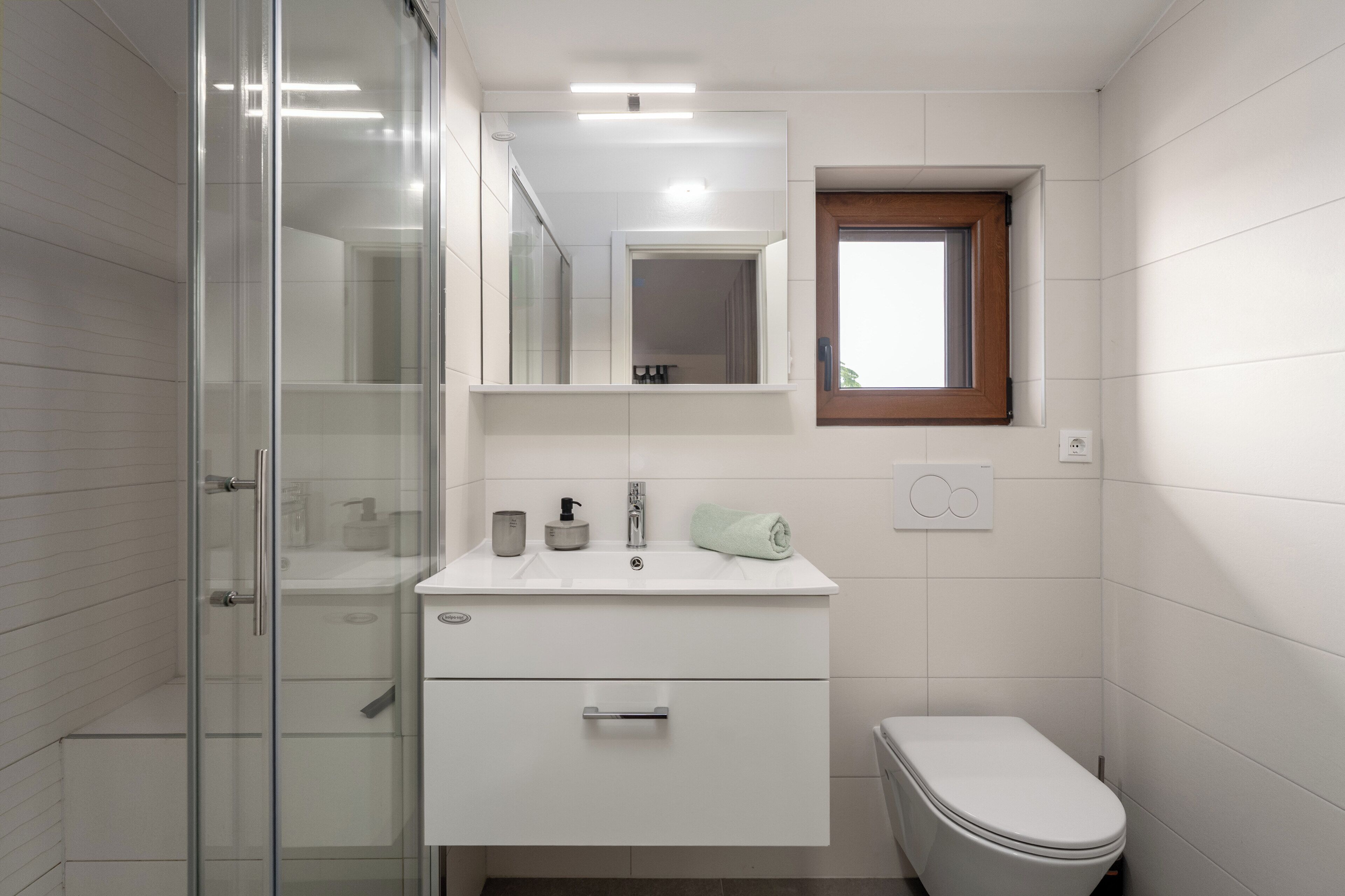 Un bagno moderno con cabina doccia in vetro, un lavabo bianco con specchio soprastante e un water.
