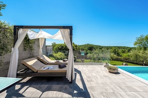Un área de piscina privada al aire libre con una pérgola, sillones de descanso y vistas al entorno vegetal.