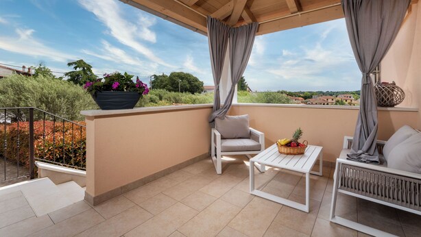 Ein überdachter Balkon mit einem weißen Stuhl, einem kleinen Tisch mit Obst und einer Topfpflanze.